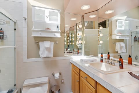 A well-lit bathroom featuring a sink with amber bottles and a shower enclosure.