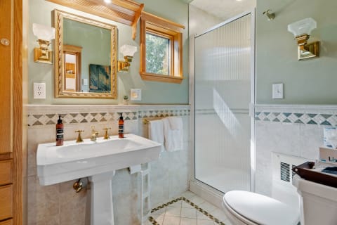 Quaint bathroom with a pedestal sink, decorative mirror, and a frosted glass shower.