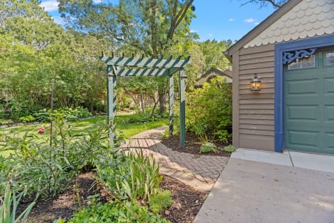 A garden pathway with a green arbor and a rustic structure nearby.