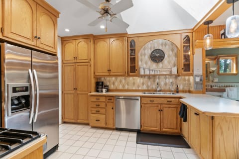A modern kitchen featuring oak cabinetry, stainless steel appliances, and a diamond-patterned backsplash.