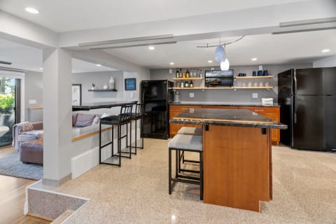 Modern kitchen featuring a dark granite island, black refrigerator, and open shelving with decorative items.