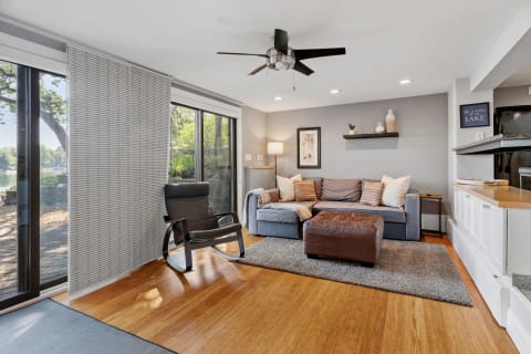 Modern living room with a sectional sofa, rocking chair, and large windows revealing a view of a lake.