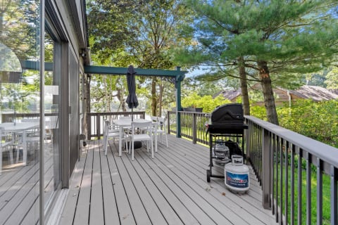 Outdoor deck featuring a white dining set, a black grill, and surrounded by trees.