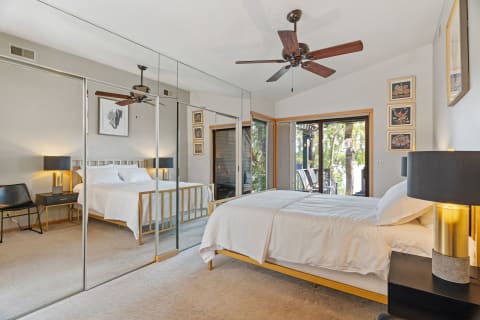 A serene bedroom with a light wood bed, black lamps, and a view of the outdoors through glass doors.