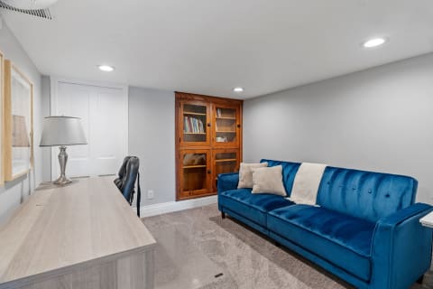 A small office space featuring a blue velvet couch, wooden desk, and a vintage book cabinet.