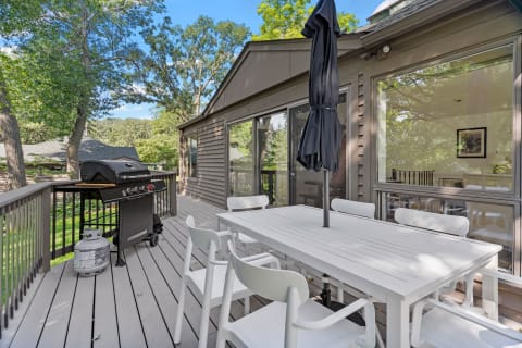 Outdoor deck with a white dining table, chairs, and a grill under a blue sky.