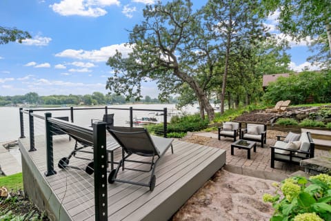 Lakeside patio with modern furniture and lush greenery in the background.