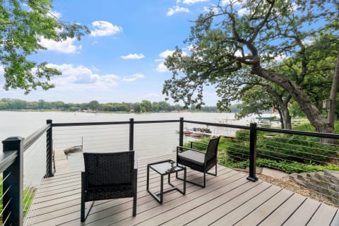 Outdoor deck overlooking a calm river with wicker chairs and greenery.