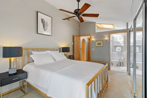 Modern bedroom with a golden bed frame, black lamps, and adjoining bathroom visible.