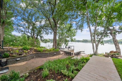 Lakeside garden with seating area, cobblestone path, and string lights among trees.