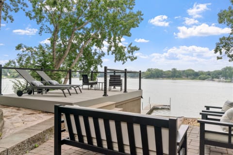 Lakeside deck with lounge chairs, a table, and a view of the water.