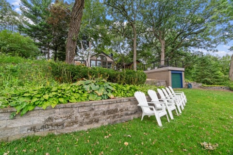 A serene outdoor area featuring white Adirondack chairs along a stone wall with vibrant plants.