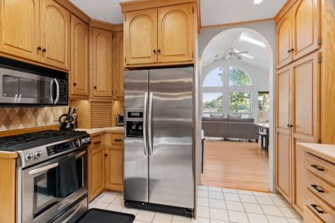 Modern kitchen with oak cabinets and stainless steel appliances leading to a light-filled living area.
