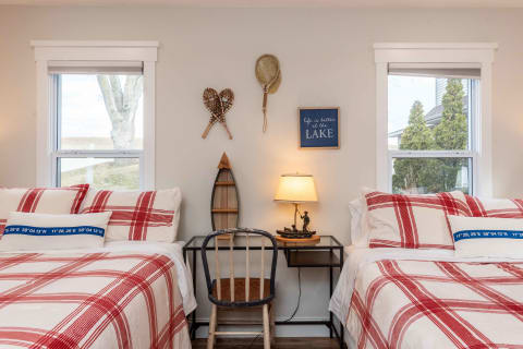 A bedroom with twin beds featuring red plaid bedding and lake-themed decor.