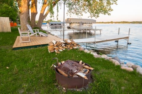 Lakeside view featuring Adirondack chairs, a fire pit, and boats on calm water.