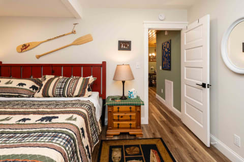 A rustic bedroom featuring a red wooden bed, nature-themed bedding, and a warm lamp on a nightstand.