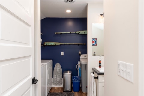 A contemporary laundry room showcasing a navy wall, modern washer and dryer, and decorative wooden paddles.