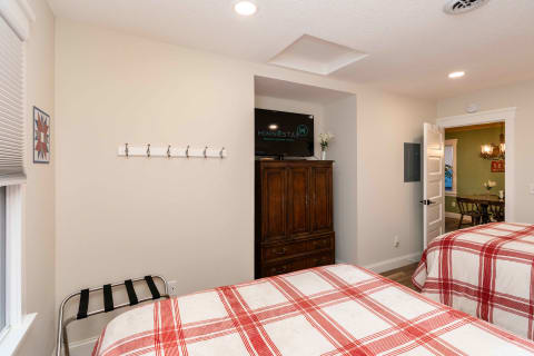 A cozy bedroom with two plaid beds and a wooden armoire containing a TV.