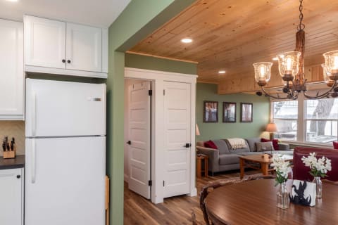 An open-concept room featuring a kitchen with white cabinets and a cozy living area with a grey couch and chandelier.