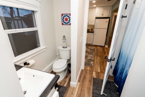 A compact bathroom with a white toilet, sink, and a view into a kitchen.