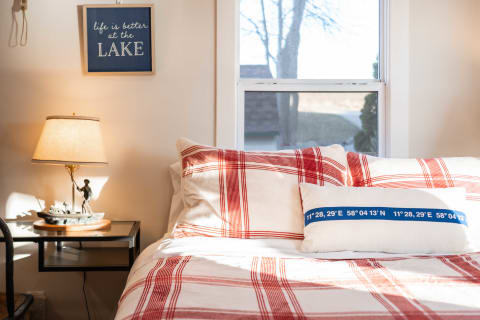 Cozy bedroom with a plaid comforter, decorative pillows, and a lamp on a side table.