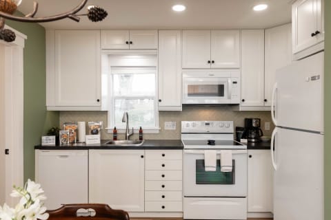 A modern kitchen featuring white cabinetry, a black countertop, and various kitchen appliances in a stylish arrangement.