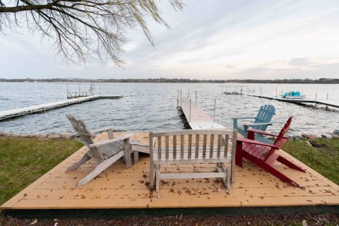Adirondack chairs on a wooden platform by the lake leading to a dock.