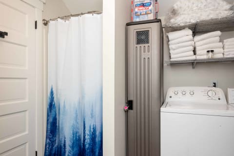 Laundry area with a forest shower curtain, stacked white towels, and a washing machine.