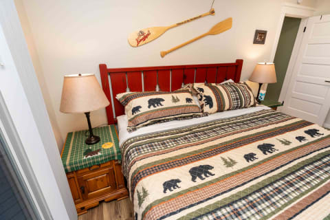 A rustic bedroom with a red bed frame, bear-themed bedding, and a wooden nightstand with a lamp.