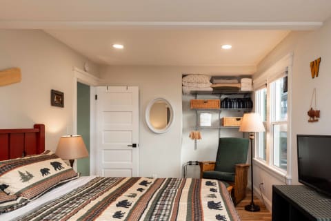 A cozy rustic bedroom with a red bed, bear-themed quilt, green armchair, and organized shelving.