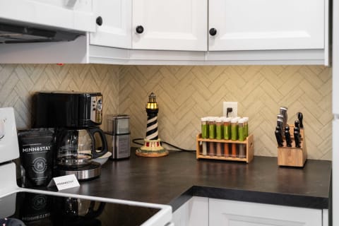 A modern kitchen corner featuring a coffee maker, stylish spice containers, and a lighthouse lamp on a black countertop.
