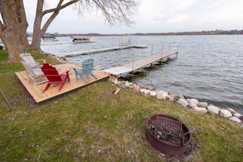 Lakeside view with colorful Adirondack chairs, a dock, and a fire pit.