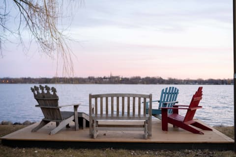 Three wooden chairs on a lakeside deck at sunset with soft colors in the sky.