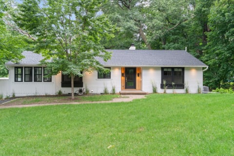 A single-story house with a black front door and large windows, set against a backdrop of greenery.