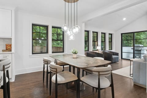 Modern dining room featuring a marble table and contemporary lighting with views of greenery outside.