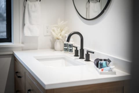 A modern bathroom with a white countertop, black faucet, and neatly arranged toiletries.