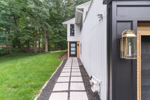 Pathway of large concrete stones bordered by black stones, leading to a contemporary home amidst trees.