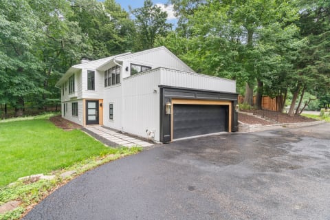 Two-story modern house with a black garage, surrounded by trees and a green lawn.