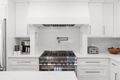 A bright and modern kitchen with white cabinets, a gas stove, and a coffee machine.