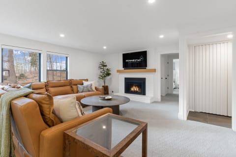 Modern cozy living room with a brown leather sectional and a white brick fireplace.