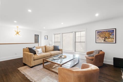 A modern living room with a tan sofa, armchairs, and a glass coffee table under a unique chandelier.