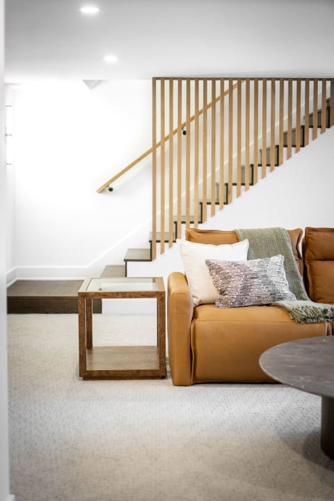 Modern basement area with a leather sofa, decorative cushions, and a staircase.