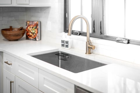 Stylish kitchen sink with brushed brass faucet and black sink on white countertop.