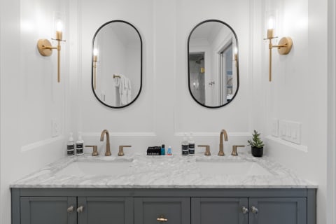 A modern bathroom vanity with a double sink and marble countertop, featuring gold fixtures and oval mirrors.
