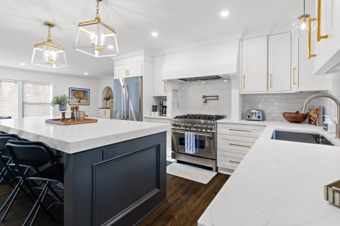 Contemporary kitchen with marble countertops, black folding chairs, and stainless steel appliances.