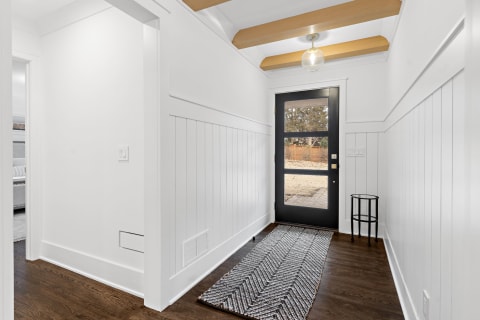 Modern entryway with white walls, wooden beams, and a black front door.