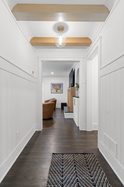 Modern hallway with white paneling and wooden beams, leading to a living room.