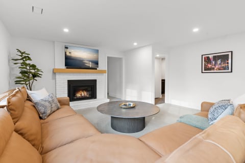 A modern living room with a leather sectional, fireplace, and a large TV displaying a beach scene.
