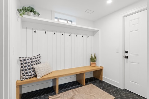 Stylish entryway featuring a wooden bench, decorative pillows, and coat hooks on a white panel wall.