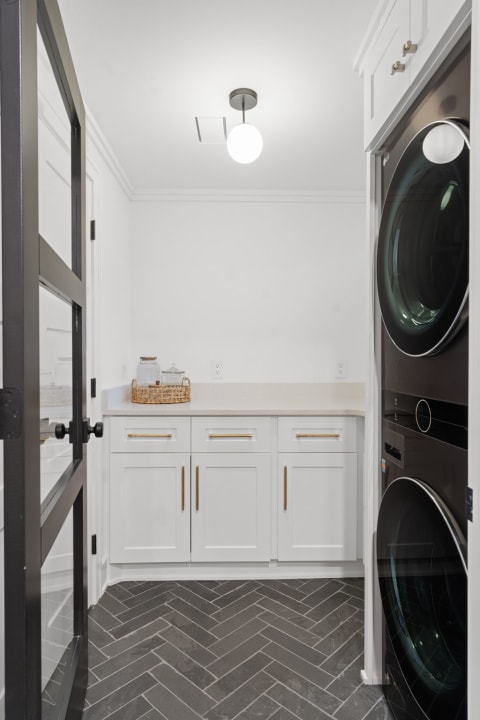Contemporary laundry room featuring white cabinets, a beige countertop, and herringbone tile flooring.